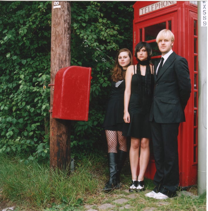 The band photographed beside red telephone boxes in long grass.