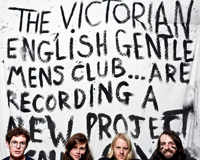 The band holding a hand-lettered sign reading that they are recording a new project.