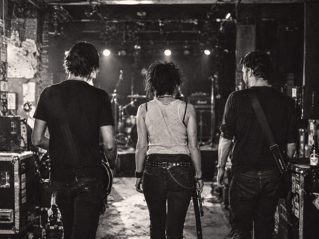 An AI-generated photoreal image of three musicians walking towards a lit stage.